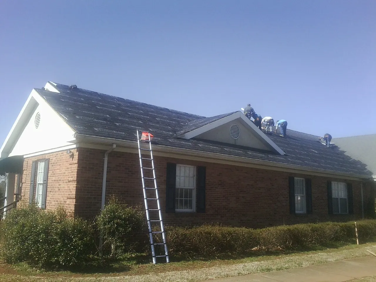 Crew tearing shingles off a brick ranch roof with a ladder set — Metal Roof Repair work by our crew in Erwinna