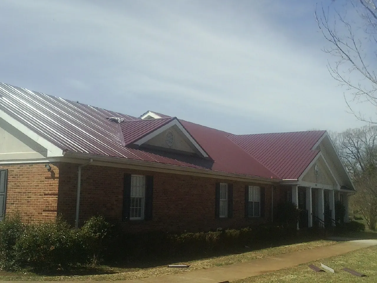 Red metal roof with gabled entries on a long brick building, from a Hail Damage Roof Repair job in Erwinna