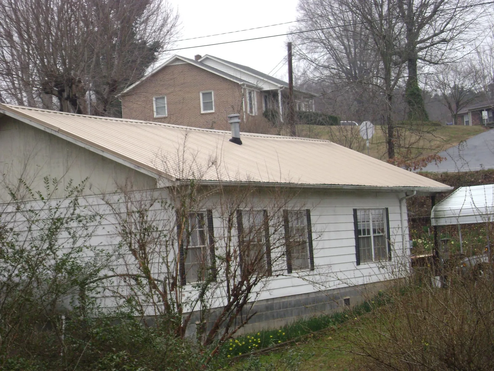 Tan metal roof on a white sided house set into a hillside — Commercial Roofing by Roofing Brothers in Erwinna
